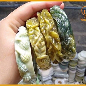 Pode incluir: Cinco pulseiras de jade esculpidas de forma intrincada em tons de verde e amarelo. As pulseiras apresentam desenhos florais e de folhas.