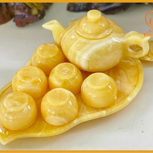 May include: A yellow marble tea set with a teapot and six cups. The set is on a leaf-shaped tray.