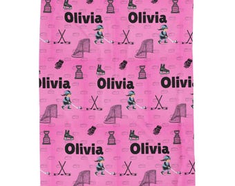 May include: Pink blanket with a repeating pattern of hockey-themed illustrations. The design includes hockey players, nets, skates, gloves, trophies, hockey sticks, and the name "Olivia".