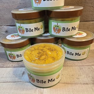 May include: Six containers of slime with a green base and a yellow top layer. The containers have brown lids and a sticker with a cartoon apple and the text "Bite Me".