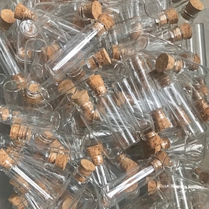 May include: A large group of small, clear glass bottles with cork stoppers. The bottles are all the same size and shape, and they are arranged in a random pattern.