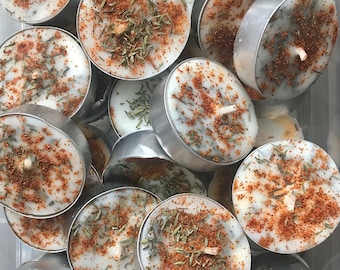 May include: A close-up of a pile of small, white tea light candles with a brown, speckled, herbal scent. The candles are in a clear plastic container.