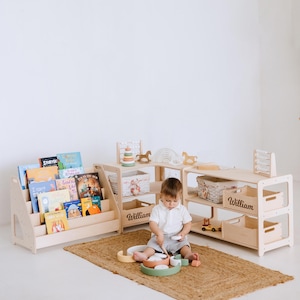 May include: A child's playroom with light wood furniture, including a bookshelf filled with colorful books, and storage shelves. The shelves have the name "William" on them. A child is playing with wooden toys on a woven rug.