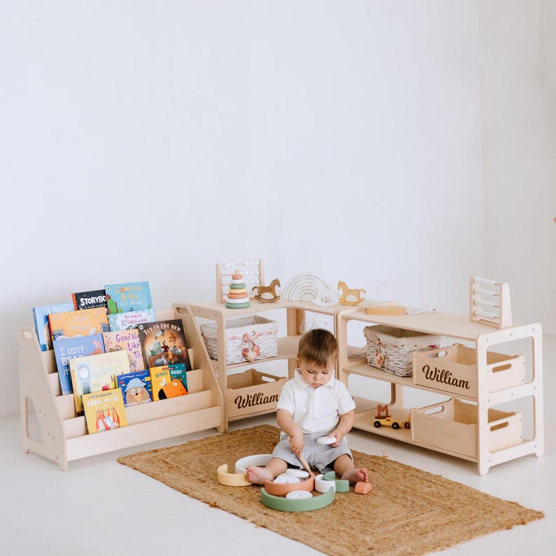 May include: A child's playroom with light wood furniture, including a bookshelf filled with colorful books, and storage shelves. The shelves have the name "William" on them. A child is playing with wooden toys on a woven rug.