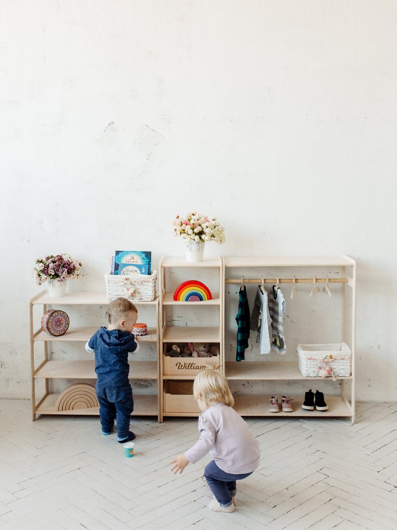 May include: Two children playing in a room with a wooden shelf unit. The shelf unit has a rainbow toy, a basket of toys, and a clothes rack. The shelf unit is labeled "William".