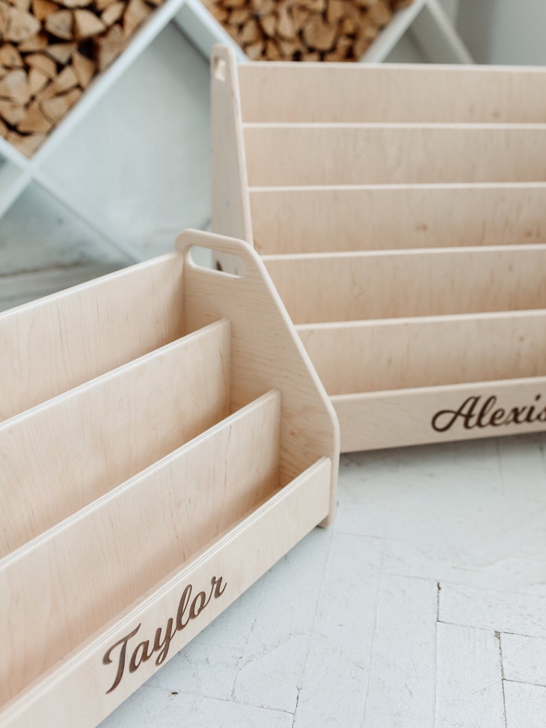 Pu&ograve; includere: Due librerie in legno con nomi personalizzati, "Taylor" e "Alexis", sono mostrate su un pavimento bianco. Le librerie sono in legno chiaro e hanno un design semplice.