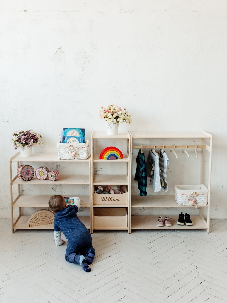 May include: A wooden shelf unit with a rainbow toy, a basket of toys, and a wooden box labeled "William". A child is playing with toys on the floor in front of the shelf.