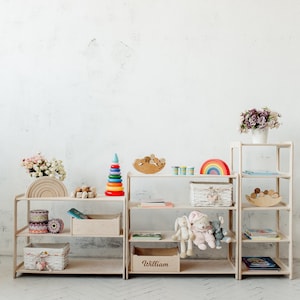 May include: Three wooden shelves with various toys and books. The shelves are labeled "William". The shelves are white and have a natural wood finish. The toys include a rainbow, a stacking ring tower, a wooden rainbow, and a wooden rocking horse. The books are colorful and have various titles.