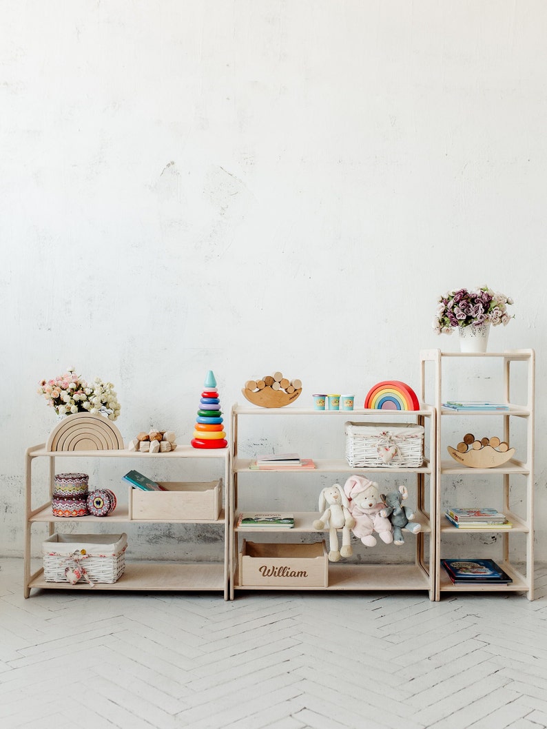 May include: Three wooden shelves with various toys and books. The shelves are labeled "William". The shelves are white and have a natural wood finish. The toys include a rainbow, a stacking ring tower, a wooden rainbow, and a wooden rocking horse. The books are colorful and have various titles.