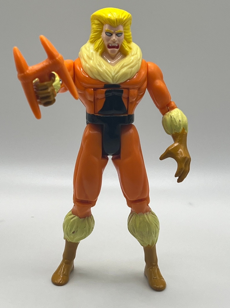 Puede incluir: Una figura de acci&oacute;n naranja y amarilla de Sabretooth de los X-Men. Est&aacute; sosteniendo un par de garras naranjas en su mano derecha. Lleva un cintur&oacute;n negro y un collar de piel amarilla.