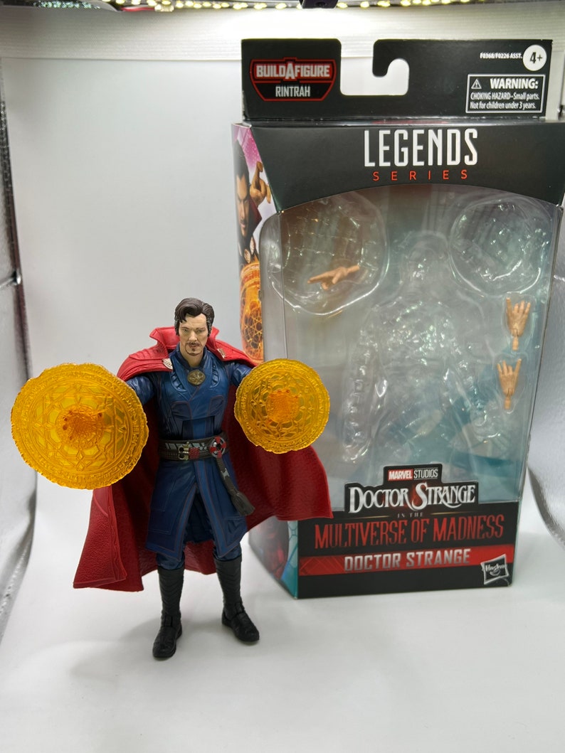 May include: Doctor Strange action figure from the Marvel Legends Series, holding two golden magic rings. The figure is wearing a red cape, blue robe, and black boots. The packaging features the Marvel Studios logo and the text "Doctor Strange in the Multiverse of Madness".