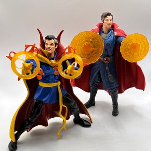 May include: Two action figures of Doctor Strange, one in a red and blue robe with a yellow sash, holding two golden rings, and the other in a red and blue robe with a yellow sash, holding two golden discs.