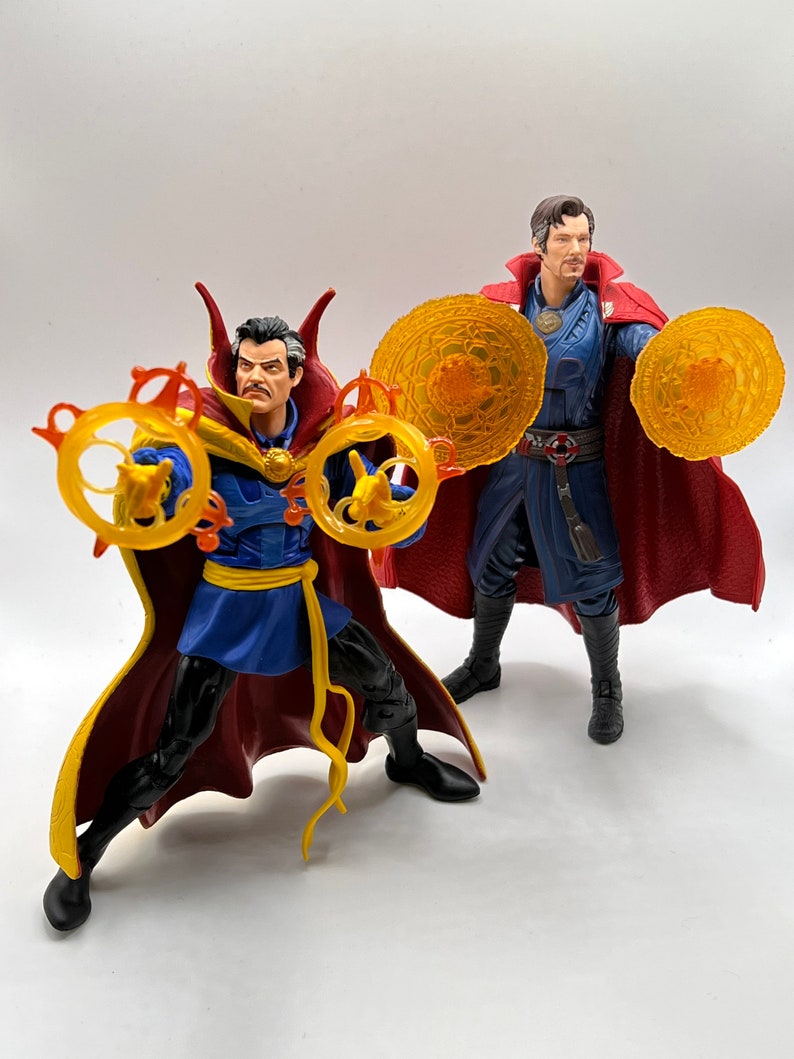 May include: Two action figures of Doctor Strange, one in a red and blue robe with a yellow sash, holding two golden rings, and the other in a red and blue robe with a yellow sash, holding two golden discs.