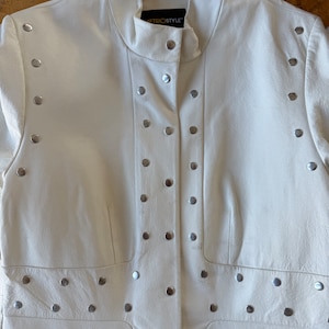 May include: A white leather jacket with silver studs. The jacket has a mandarin collar and a button closure. The label on the jacket reads "Metrostyle".