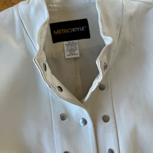 May include: White leather jacket with a stand-up collar and a button closure. The jacket has a Metrostyle label with the text "Genuine Leather Exclusive of Decoration Professional Leather Clean 20-0219-3 Size 14 Made in China".