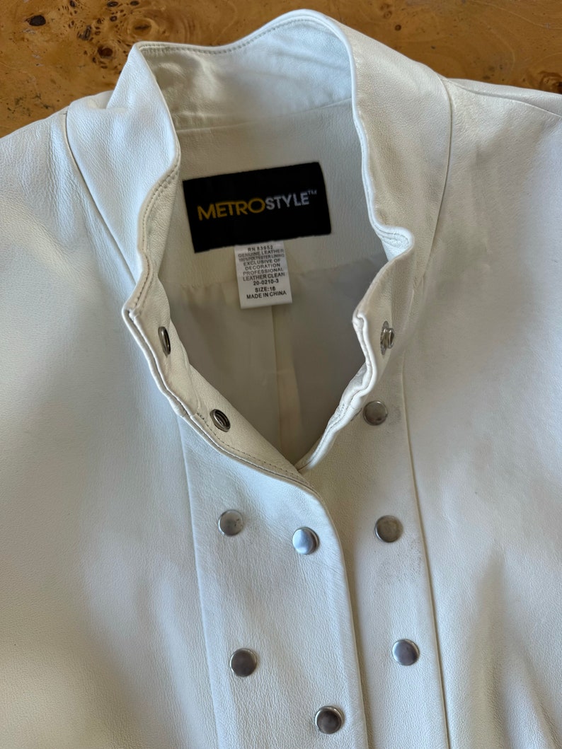 May include: White leather jacket with a stand-up collar and a button closure. The jacket has a Metrostyle label with the text "Genuine Leather Exclusive of Decoration Professional Leather Clean 20-0219-3 Size 14 Made in China".