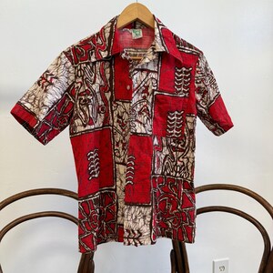 May include: A red, white, and brown short-sleeved button-up shirt with a geometric pattern. The shirt has a collar and a button closure.