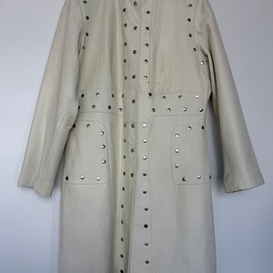 May include: A white leather jacket with silver studs. The jacket has a stand-up collar and long sleeves.