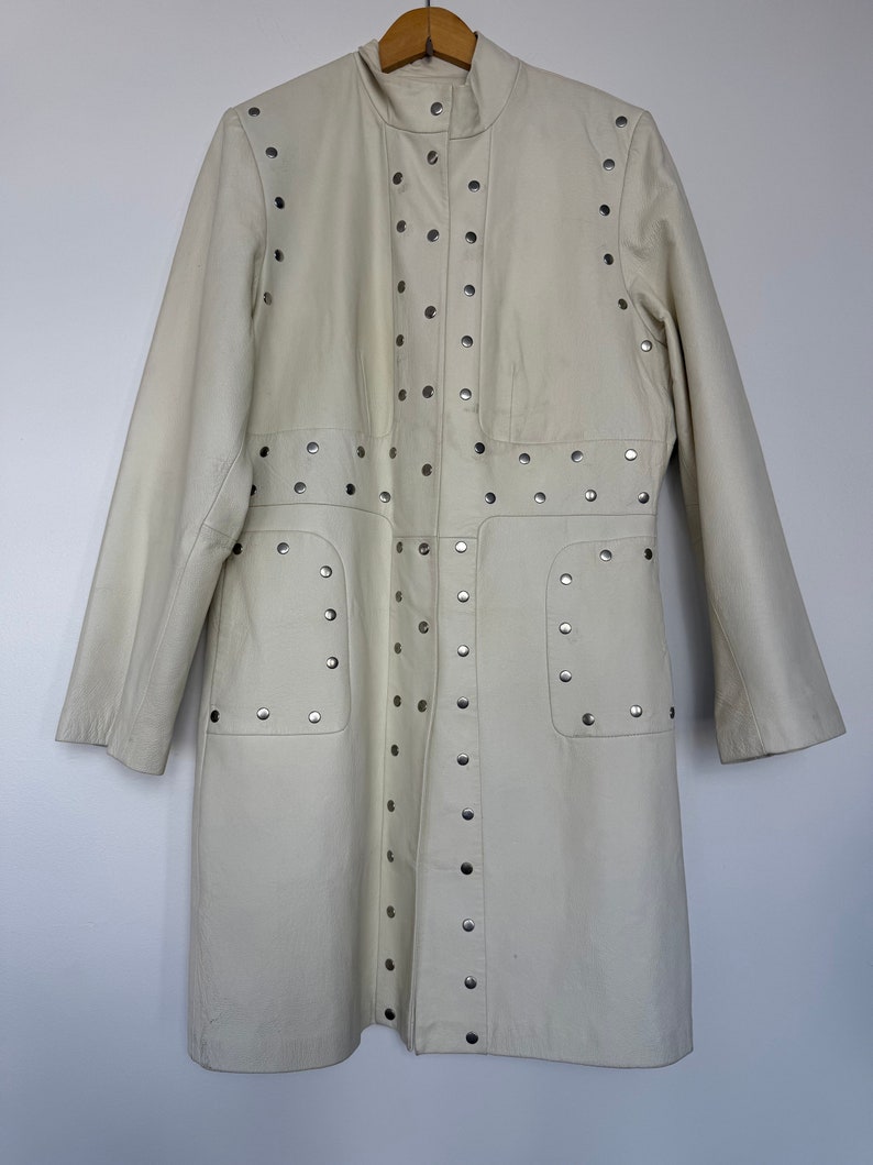 May include: A white leather jacket with silver studs. The jacket has a stand-up collar and long sleeves.