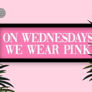 May include: A pink sign with black framing and white text that reads "On Wednesdays We Wear Pink" against a pink background with green palm leaves on either side.