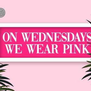 May include: A white framed sign with a pink background and the text "ON WEDNESDAYS WE WEAR PINK" in white letters.