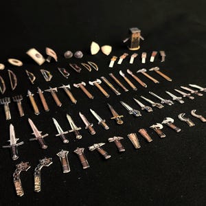 May include: A collection of miniature toy weapons, including swords, axes, hammers, and other medieval-themed tools. The toys are made of paper and wood, with brown and silver tones, arranged on a black surface.