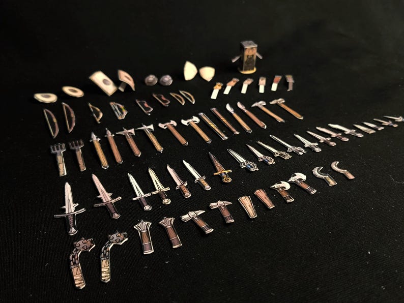 May include: A collection of miniature toy weapons, including swords, axes, hammers, and other medieval-themed tools. The toys are made of paper and wood, with brown and silver tones, arranged on a black surface.