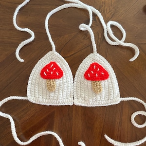 May include: White crocheted bikini top with red and white mushroom appliques.