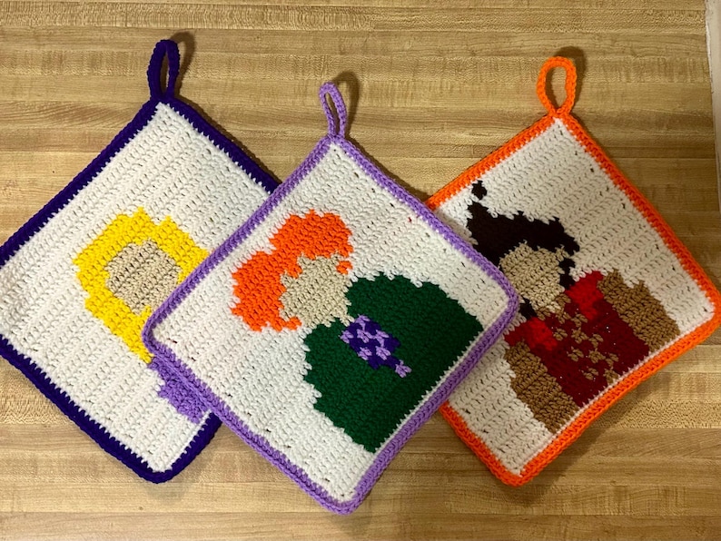 May include: Three crocheted pot holders featuring different characters. The first pot holder is purple and features a yellow character. The second pot holder is lavender and features an orange character with green and purple clothing. The third pot holder is orange and features a brown character with red and brown clothing.