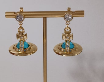 Vivienne Westwood- Boucles d'oreilles en plaqué or avec des cristaux bleus, transparents et saturne.