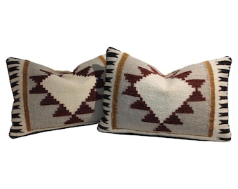 May include: Two rectangular throw pillows with a geometric design. The pillows have a cream-colored center with a dark red triangle pattern. The edges are gray with a black and gold border.