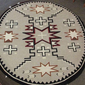 May include: A round, gray and white rug with a black border. The rug features a repeating pattern of stars and crosses. The center of the rug has a larger star with a cross in the middle.