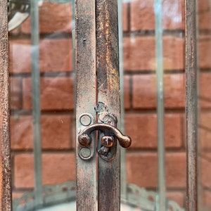 May include: A rustic metal lantern with a glass panel and a metal latch. The lantern has a distressed brown finish and a decorative design around the glass.