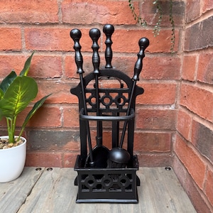 May include: Black fireplace tool set with a stand. The set includes a poker, shovel, brush, and tongs. The stand has a decorative design and holds the tools upright. The tools are made of metal and are designed for use with a fireplace.