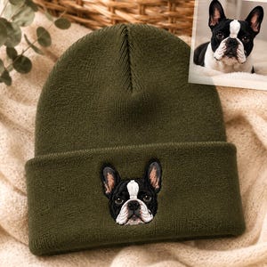 May include: An olive green knit beanie featuring a detailed embroidered patch of a black and white French Bulldog on the front cuff. The embroidery captures the dog's pointed ears, dark eyes, and white facial markings, matching the inset photo.