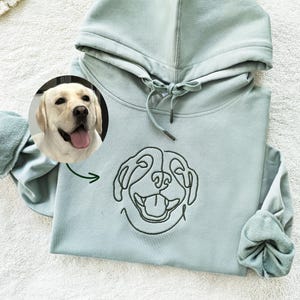 May include: A light blue hooded sweatshirt with a black line drawing of a dog's face on the front. The dog has its tongue sticking out.