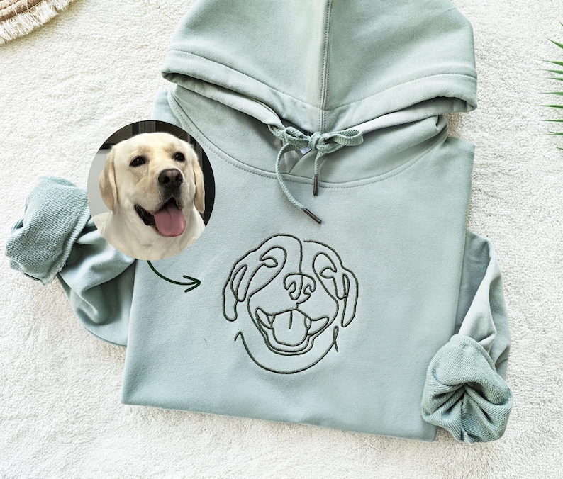 May include: A light blue hooded sweatshirt with a black line drawing of a dog's face on the front. The dog has its tongue sticking out.