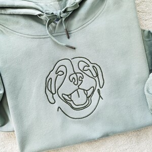 May include: A light green hooded sweatshirt with a black line drawing of a dog's face embroidered on the front.