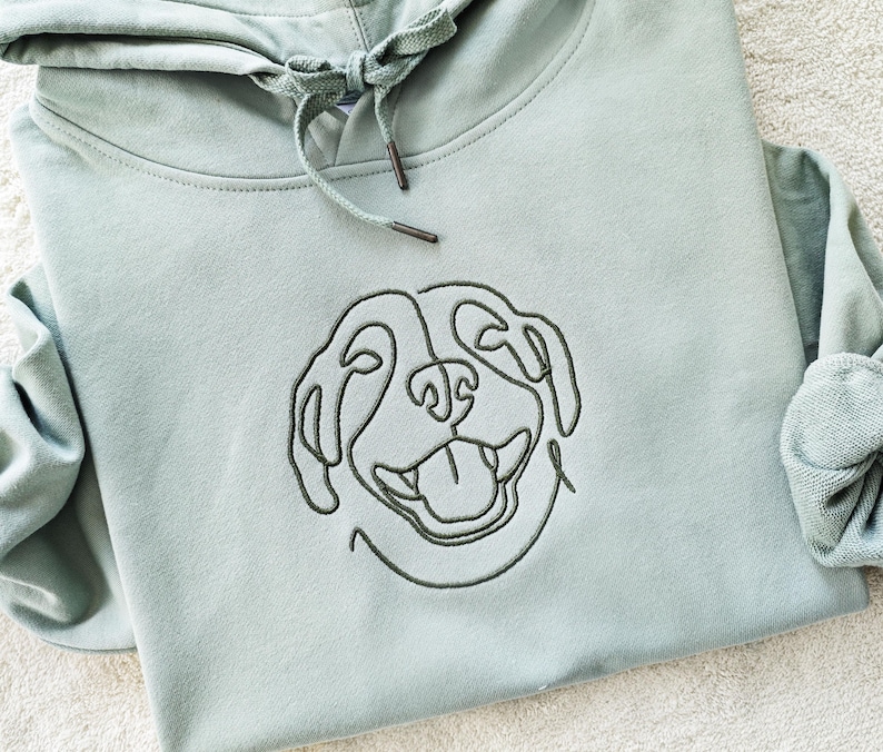 May include: A light green hooded sweatshirt with a black line drawing of a dog's face embroidered on the front.