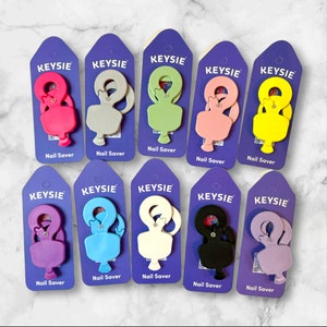 May include: Ten colourful nail savers with the brand name "KEYSIE" printed on each card. The nail savers are made of plastic and come in a variety of colours, including pink, yellow, green, blue, purple, and black.
