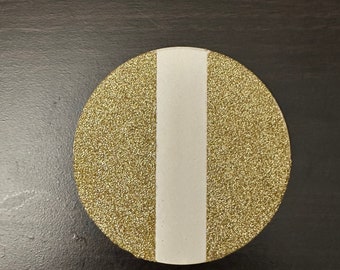 May include: A round, gold glitter coaster with a white stripe down the center.