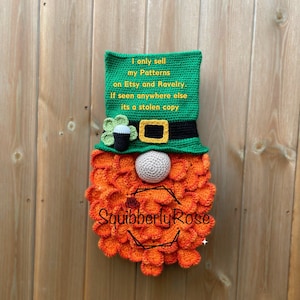 Peut inclure: Un gnome leprechaun crocheté avec un chapeau vert, une barbe orange et un trèfle. Le chapeau porte le texte "I only sell my Patterns on Etsy and Ravelry. If seen anywhere else its a stolen copy" et le texte "Squibberly Rose" est sur la barbe.
