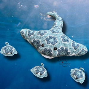 Könnte beinhalten: Ein gehäkeltes Mantarochen-Spielzeug in Blau- und Weißtönen mit einem Blumenmuster. Das Spielzeug hat schwarze Knopfaugen und wird von drei kleineren gehäkelten Mantarochen begleitet. Der Hintergrund ist eine blaue Unterwasserszene.