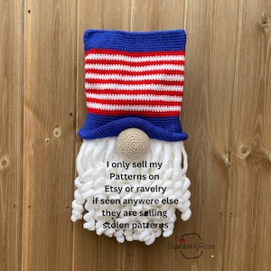 Peut inclure: Un gnome en crochet portant un chapeau rouge, blanc et bleu avec une barbe blanche. Le gnome est sur un fond en bois. Le texte "I only sell my Patterns on Etsy or ravelry if seen anywhere else they are selling stolen patterns SquibberlyRose" est écrit sous le gnome.