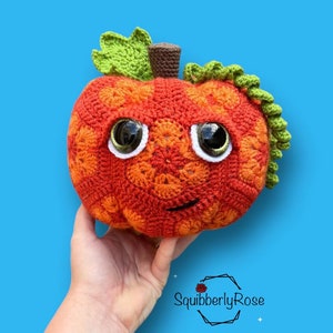 Peut inclure: Une citrouille en crochet avec une tige et des feuilles vertes, un corps orange et brun, et des yeux globuleux. La citrouille a un sourire cousu.