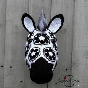 May include: A black and white crocheted zebra head mask with a black mane. The mask is made with a granny square pattern.