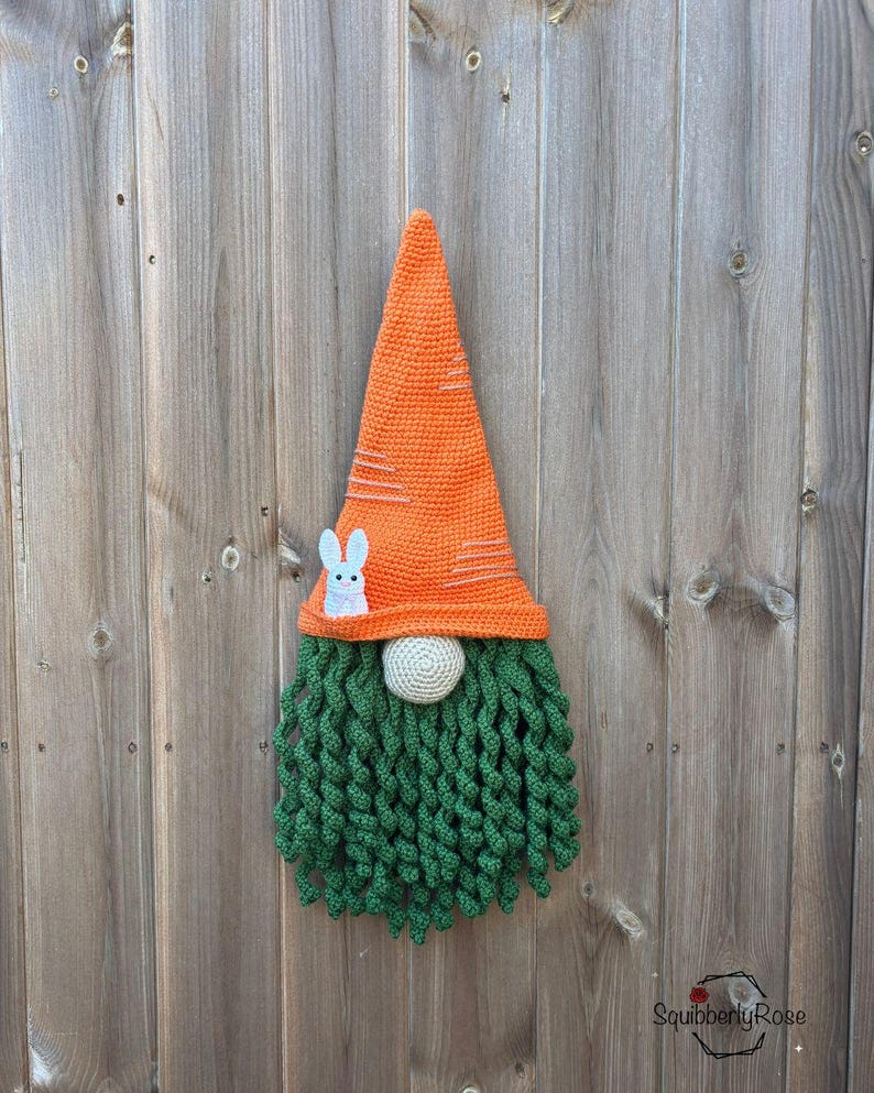 May include: A handmade crochet gnome with an orange carrot-shaped hat and a green beard. The hat has white stripes and a small white bunny applique. The gnome's nose is a light beige sphere. Perfect for Easter decor.