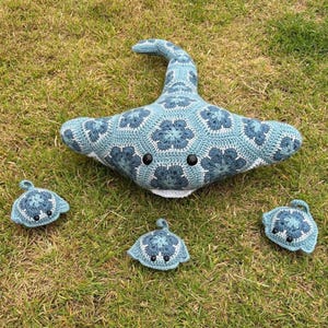 May include: A large crochet stingray plush toy accompanied by three smaller matching stingray plush toys. Each item is crafted from blue and white yarn in a hexagonal floral pattern, featuring black bead eyes and a white underside.