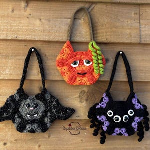May include: Three handmade crochet Halloween-themed bags. The bags are shaped like a bat, a pumpkin, and a spider. The bat bag is black and gray, the pumpkin bag is orange, and the spider bag is black and purple. Each bag has a handle.