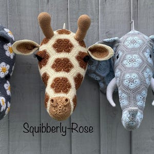 May include: Three crochet animal head wall mounts featuring a gray rhino with white and yellow flower motifs, a brown and cream giraffe with a hexagonal pattern, and a light blue and gray elephant with intricate floral crochet details. Text reads Squibberly-Rose.